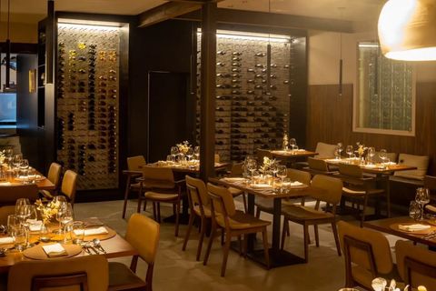 Salão do Per Lui em Belo Horizonte, com mesas postas e adegas de vinho iluminadas